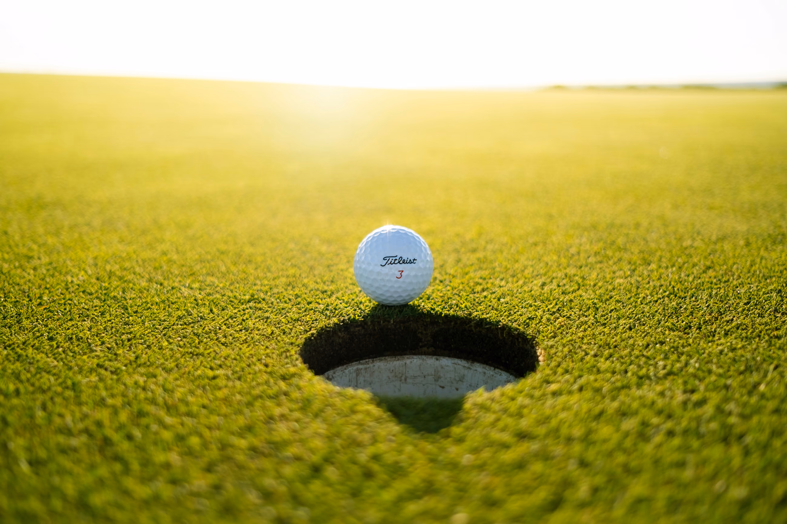 A golf ball on the lip of the hole on a sunlit green